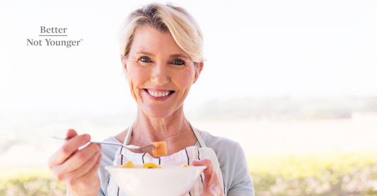 A mature woman with healthy hair is about to eat a bowl of fruits while smiling happily.
