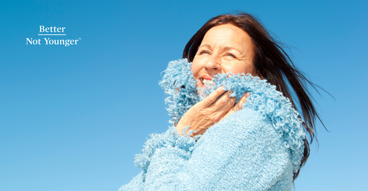 In This Article about the best hair care routine for winter, Better Not Younger features a mature woman with black long hair wearing a light blue sweater on a blue background created by the sky.