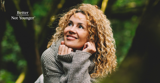 For "10 Signs You Have High Porosity Hair", Better Not Younger features a woman in her 40s with long curly hair. She smiles while appreciating the beauty of green wild nature.