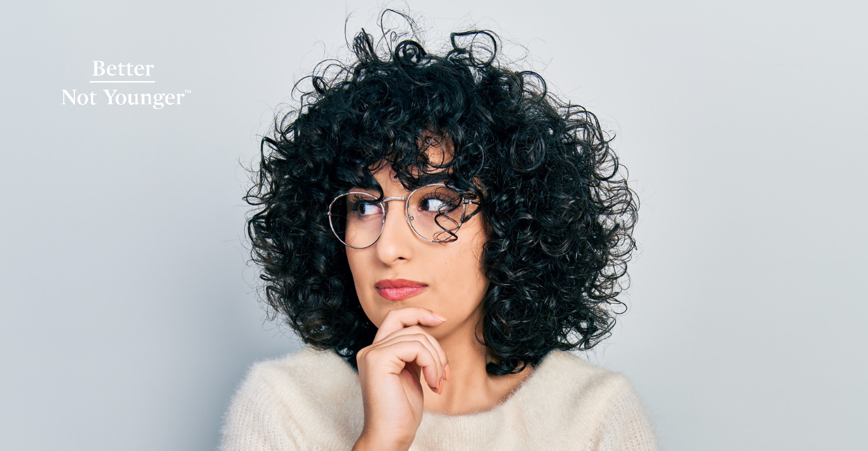100 sings of aging hair article by Better Not Younger features a woman with curly hair wearing glasses a shed looks like thinking 