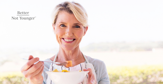 A mature woman with healthy hair is about to eat a bowl of fruits while smiling happily. 