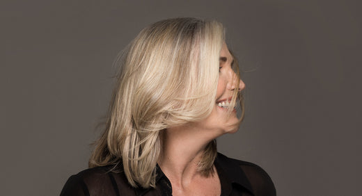 a woman over 40 years old with blonde long hair smiles and feels happy about the results of her hair care routine by better not younger