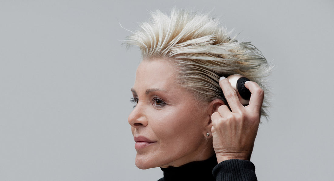 a woman over 40 years old is smiling at the camera and feeling happy about the hair regrowth benefits to her medium blonde hair by better not younger's hair serum applicator and scalp massager