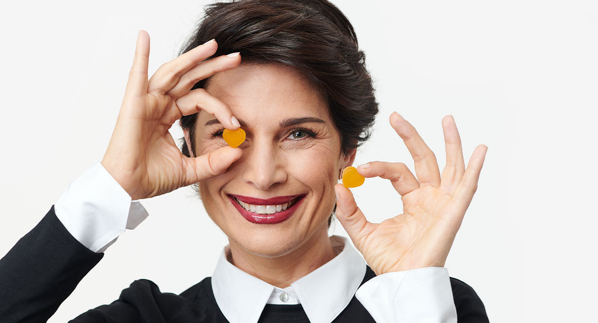 In this article "What Vitamin Should I Take for Hair Loss?", BNY features a beautiful mature woman with black short hair, holding two vitamin pills while smiling.