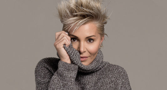 A woman over 40 years old with blonde medium haircut wears a greay sweater and looks happy about the results of her hair care routine
