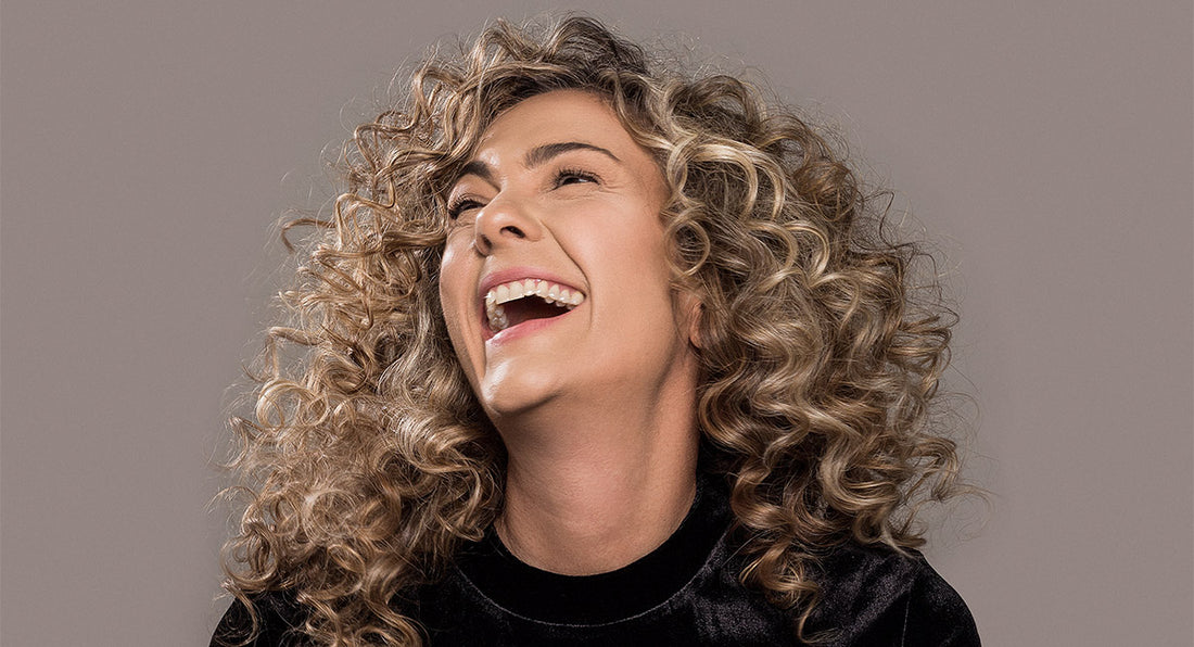 A woman over 40 years old with curly hair laughs beacuse she feels ver happy abut the results of the supplements she consumes for her hair