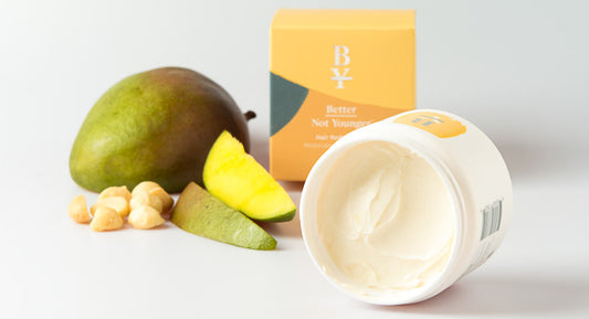 A Plant-based hair mask shows it's soft texture and it is placed next to some plant-based ingredients of it's formula like mango which work as hair restorative agents that bring some benefits like hair growth