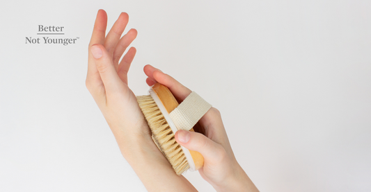 A hand holding a natural wooden brush for dry brushing her skin and body.