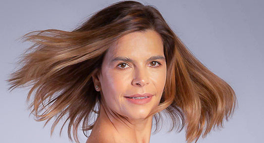 Mariela is s woman with medium haircut and in this picture she shakes her head happily showing the results of a hair growth routine. This is a headshot, very close up. Her hair looks like moving with the wind.