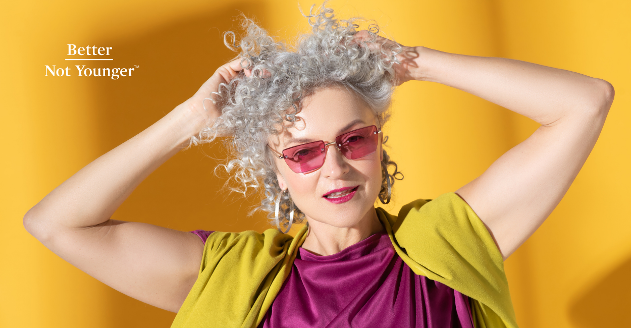 A woman with curly gray hair on a solid yellow background.