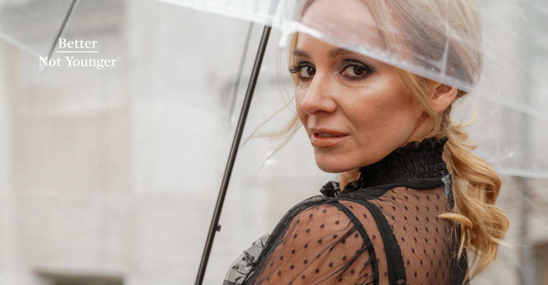 A woman over 40 holding an umbrella on a rainy day to avoid frizzy hair, pollution and more damage caused by rain on hair.