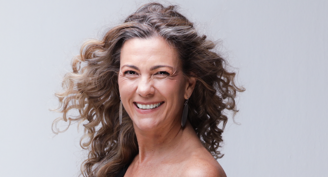 A close up of A smiling woman with beautiful curly brown hair wearing hanging earings seems to be happy about her hairstyle