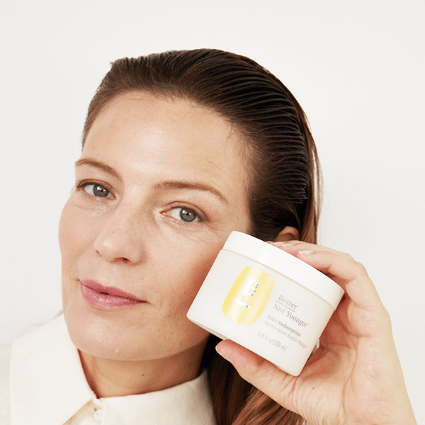 Woman holding a jar of skincare product close to her face on a white background