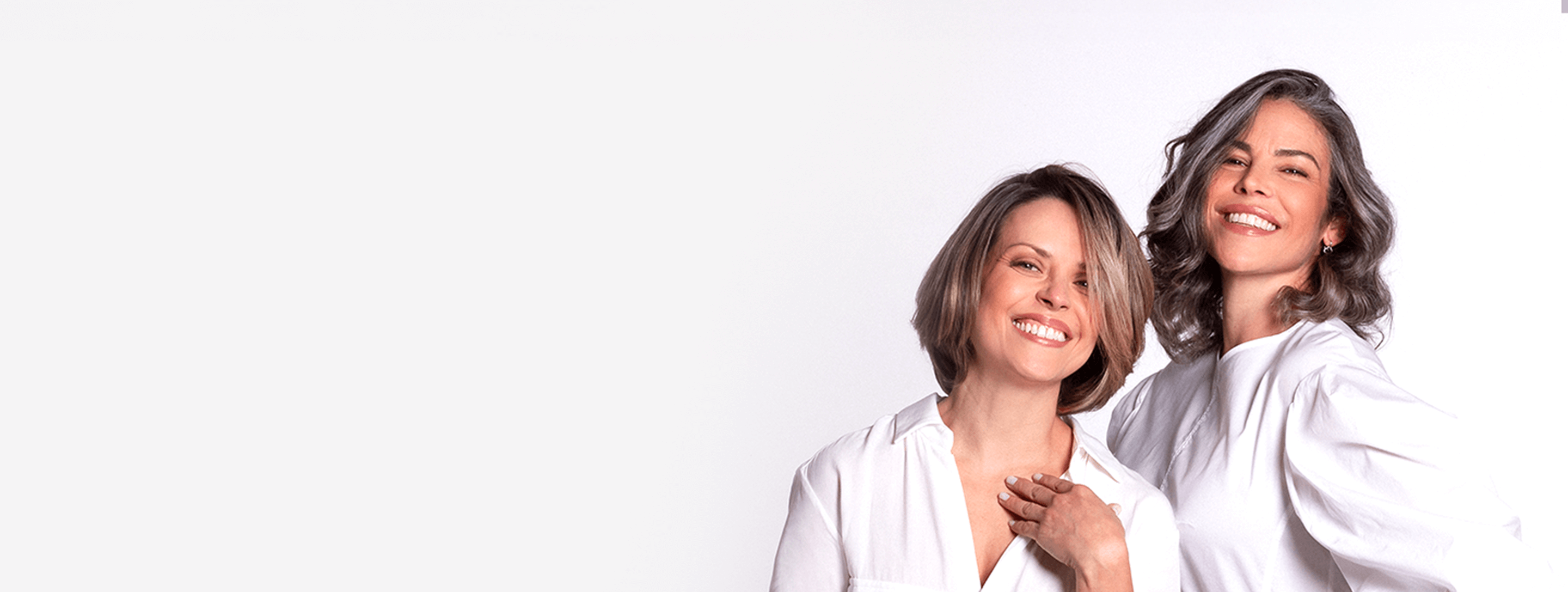 Two women in white robes standing close together on a white background