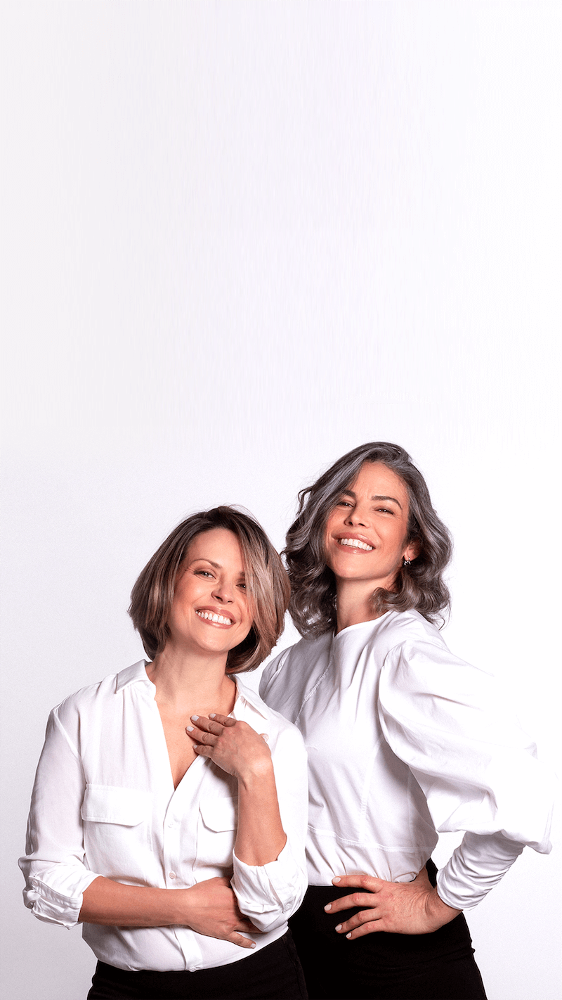 Two women wearing white shirts and black pants standing against a white background